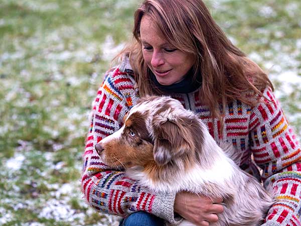 Why Take the Canine Good Citizen Test With Your Australian Shepherd? - Photo: Lady hugging red merle Australian Shepherd with snowy grass in background.