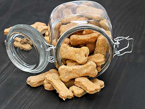 Homemade dog treats spilling from a glass jar.