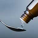 Homeopathy remedy dripping onto spoon from dark bottle
