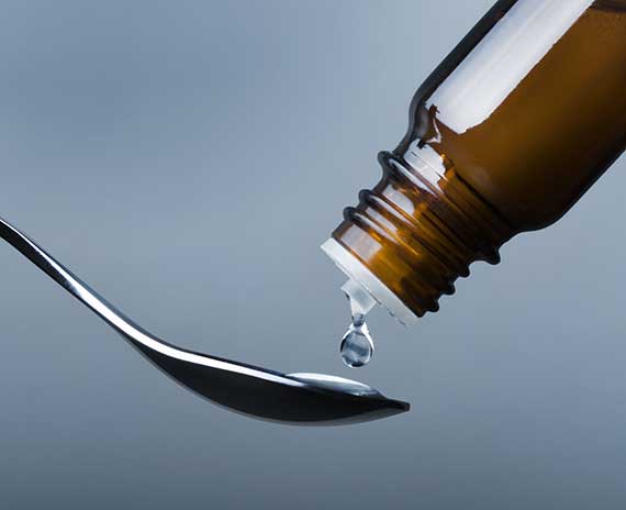 Homeopathy remedy dripping onto spoon from dark bottle