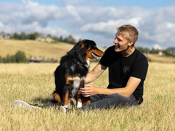 Methods of Dog Training: Finding What Works Best for You - Photo: Australian Shepherd sitting beside young man in field.